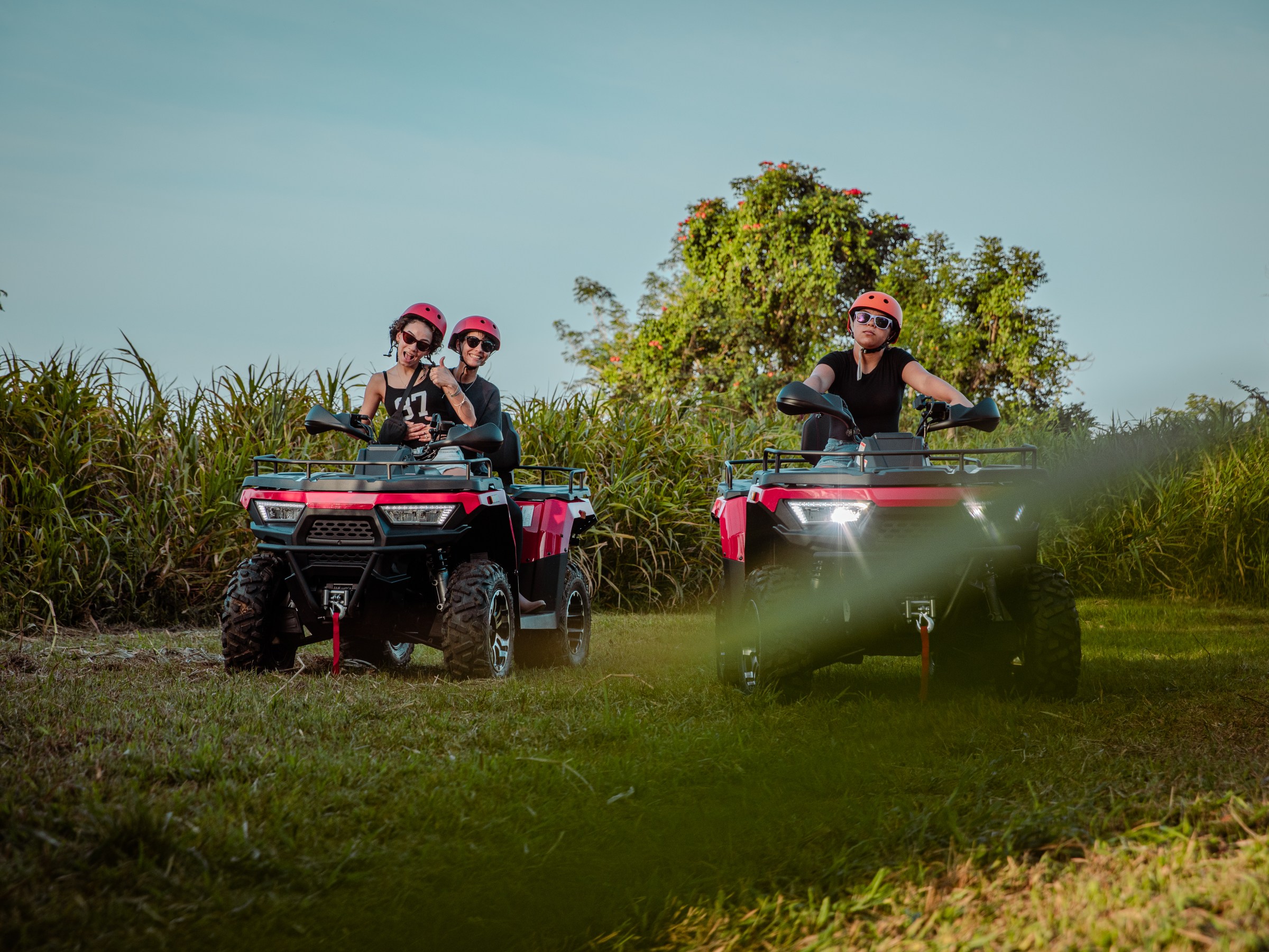 Three people on ATVs wearing helmets in a grassy area.