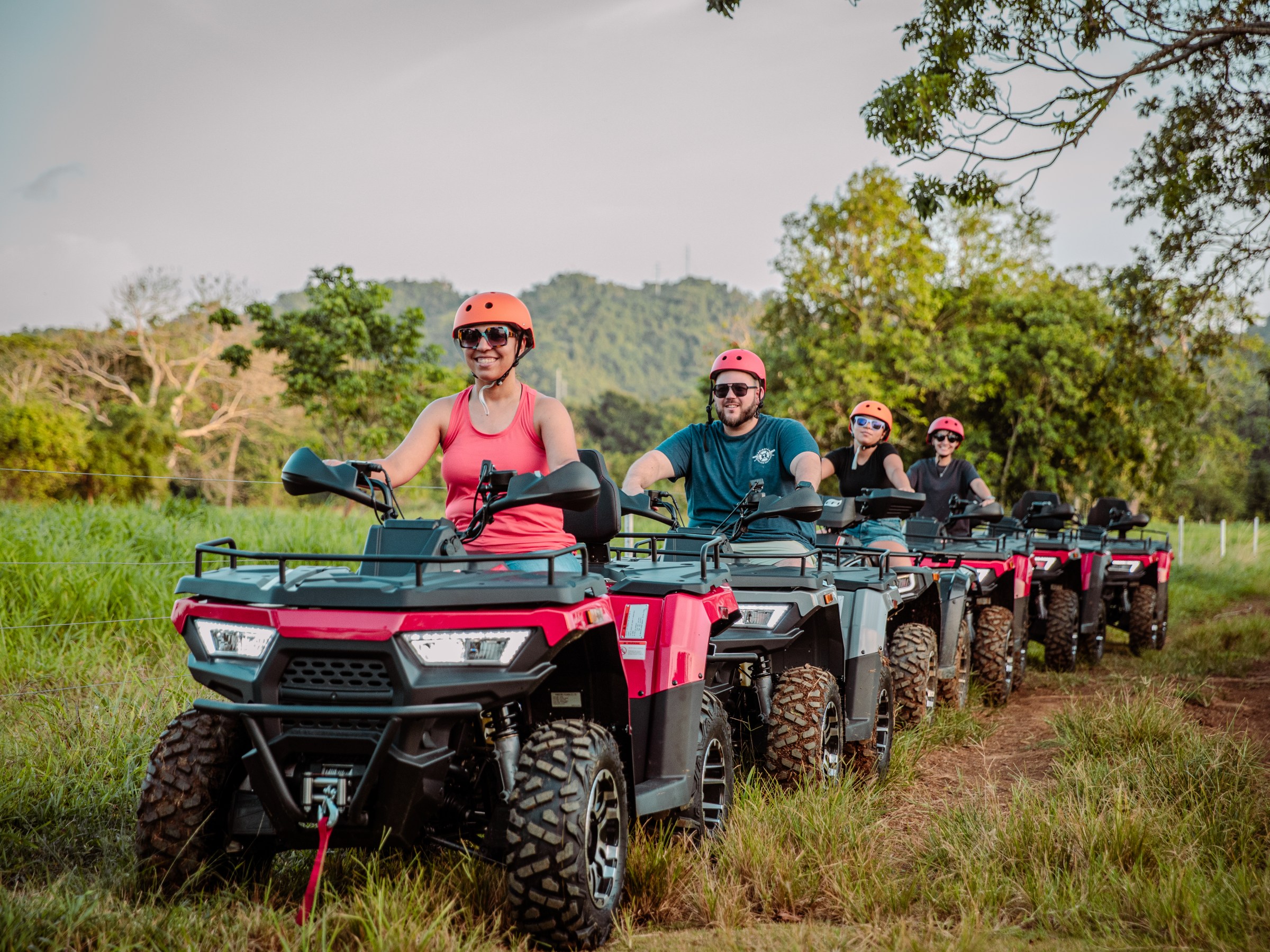 Group riding ATVs on a grassy trail with helmets on.