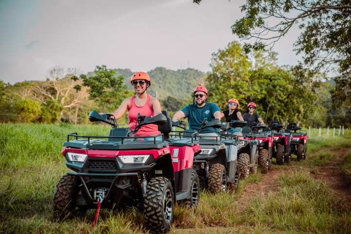 Group of people riding ATVs on a dirt path in the countryside.