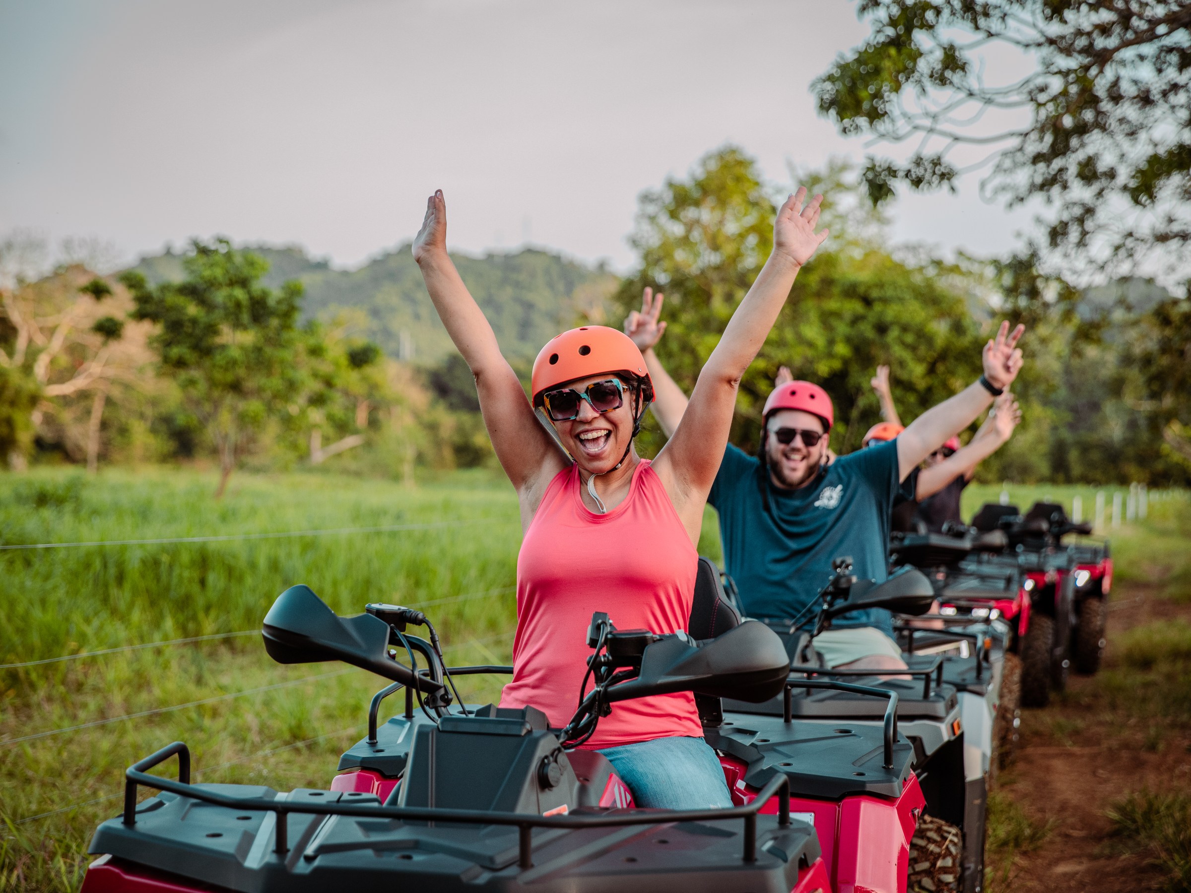 Happy people riding ATVs on a trail with trees and hills in the background.