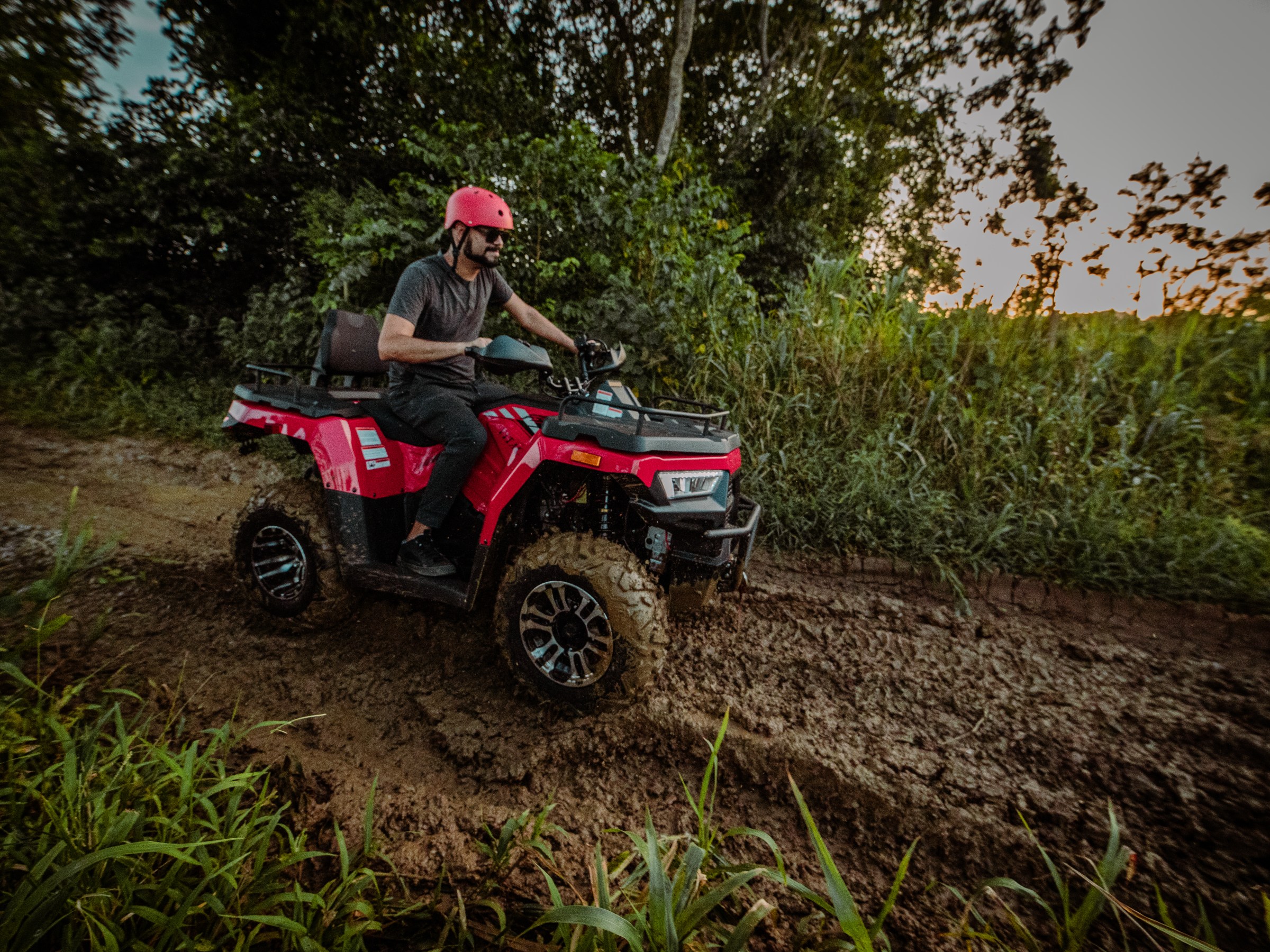 Man riding a red ATV on a muddy path in a forested area.