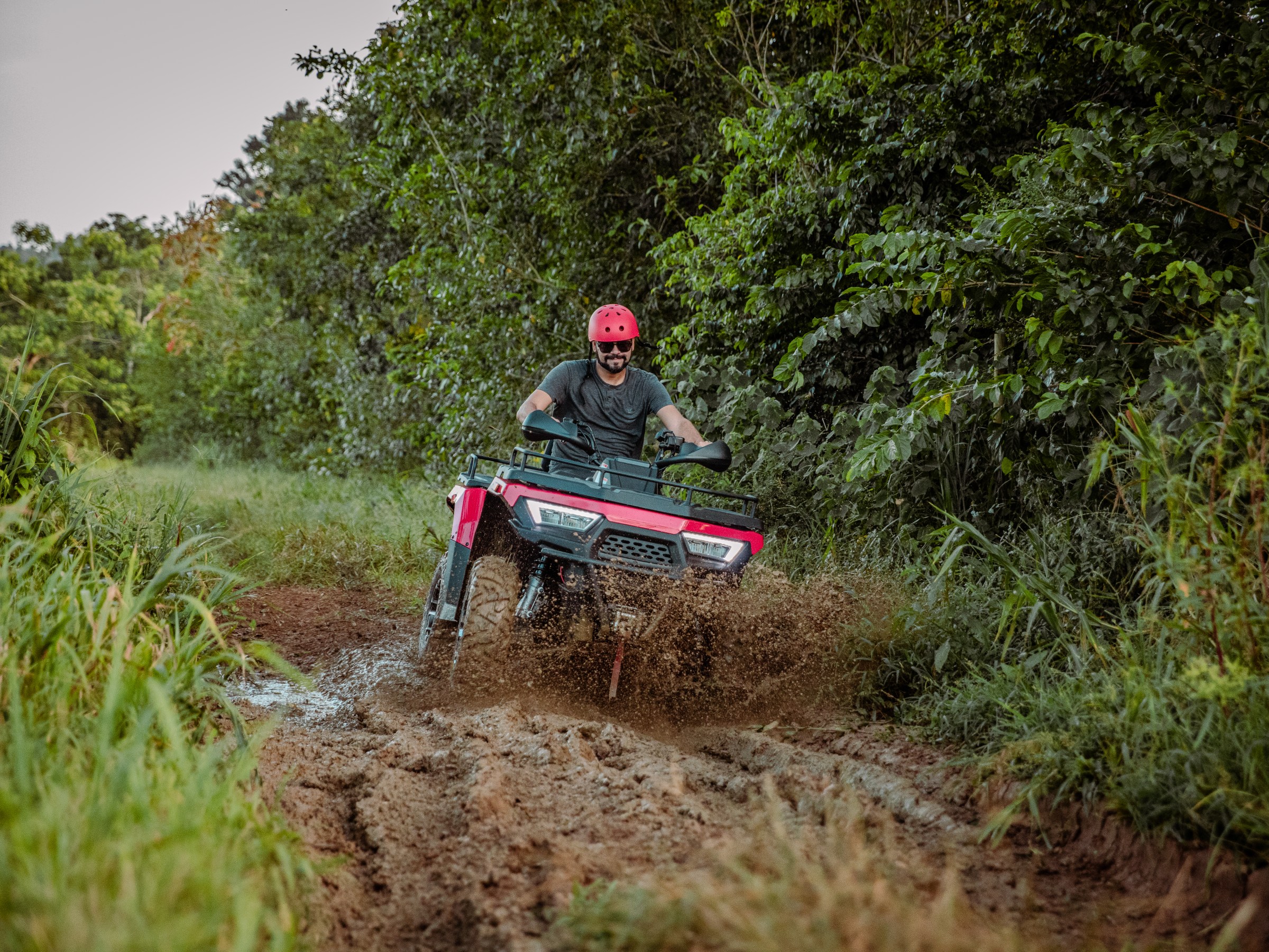 Person riding an ATV through a muddy forest trail.