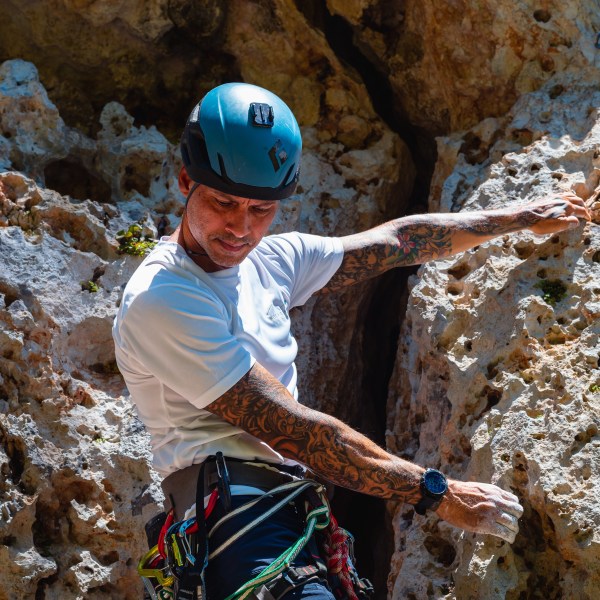 Man rock climbing with helmet and gear on rocky terrain.