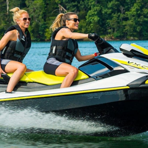 Two people on a yellow and white jet ski speeding on a lake.