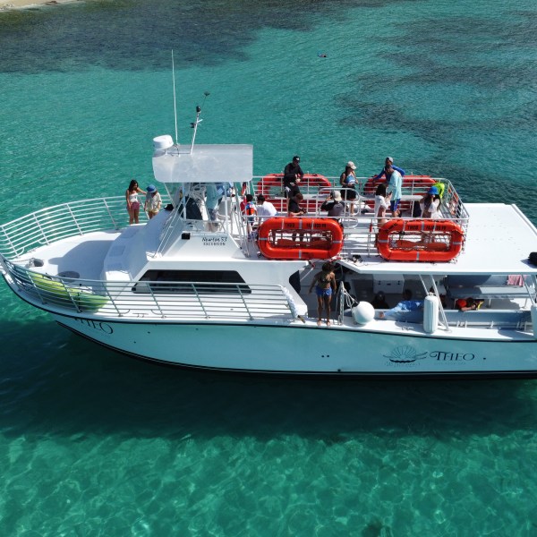 White boat with people in clear turquoise water near shoreline.