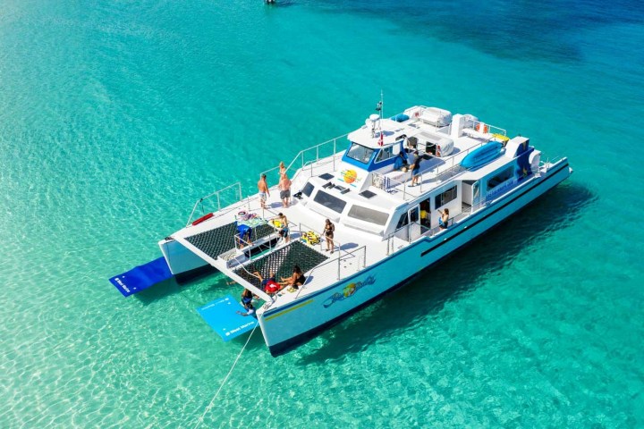 Catamaran with people on turquoise sea, clear sky.