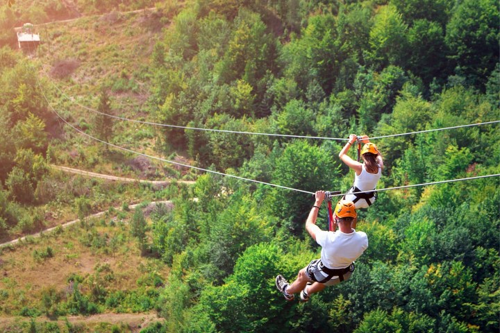 Two people zip-lining over a forested area.