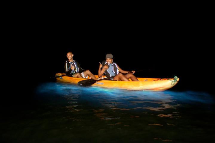 Two people kayaking at night with glowing water.