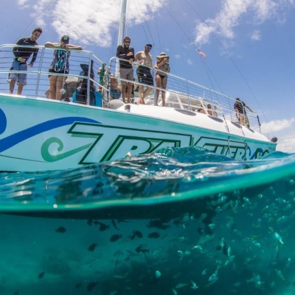 People on a boat above clear water with fish visible below.