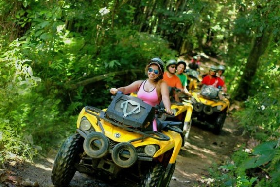 Group riding yellow ATVs through lush forest trail.