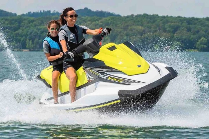 Two people riding a yellow and white jet ski on a lake.