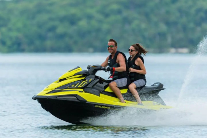 Two people riding a yellow jet ski on a lake.