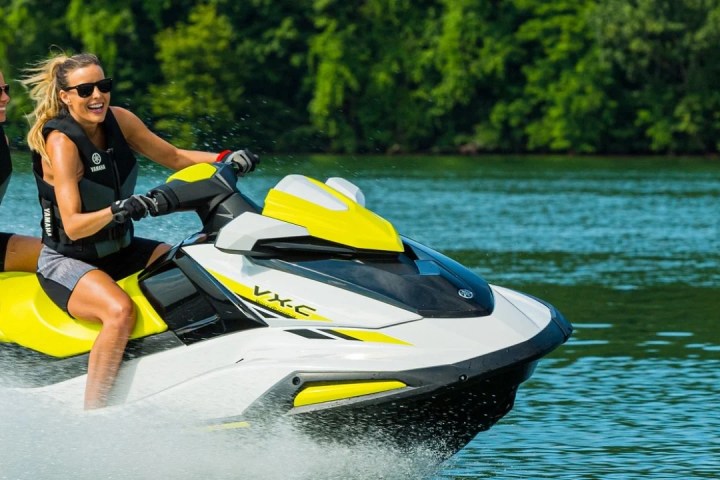 Two people riding a yellow and white jet ski on a lake.