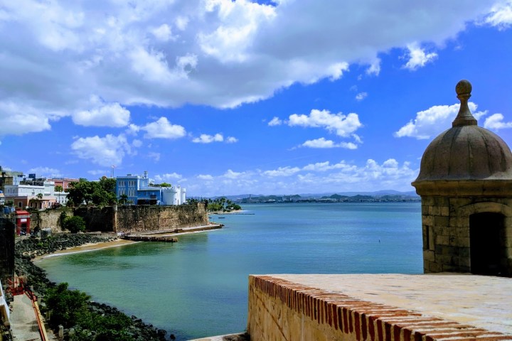 Coastal view with historic fort, ocean, and cloudy blue sky.