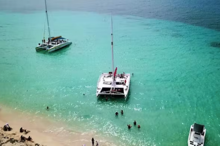 Catamarans and people in turquoise water near a sandy beach.