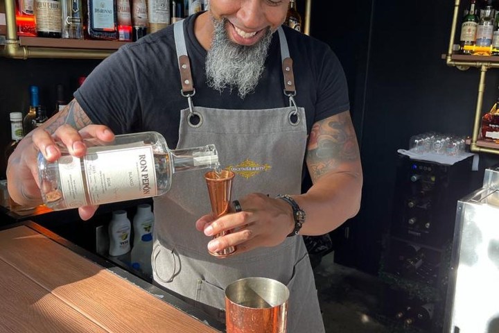 Smiling bartender pouring liquor into a jigger at a bar.