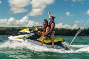 Two people riding a yellow and white jet ski on clear blue water.