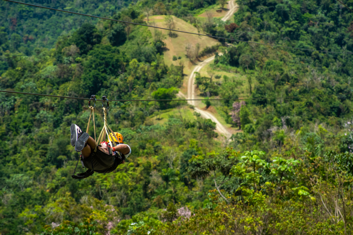 Person zip lining over lush green hills and forested landscape.