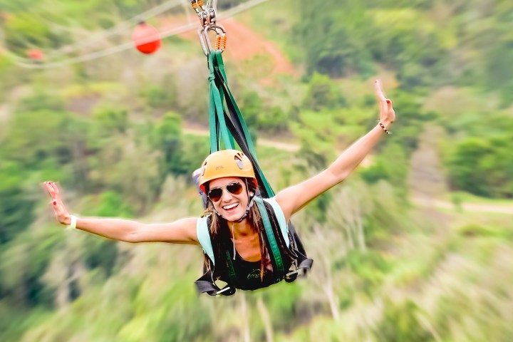 Person ziplining with arms outstretched over a blurred green landscape.