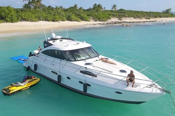 White yacht near beach, jet ski and people sunbathing.