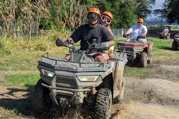 Group of people riding ATVs through a muddy trail on a sunny day.