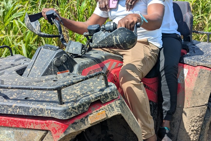 Two people in helmets enjoying an ATV ride through grassy terrain.