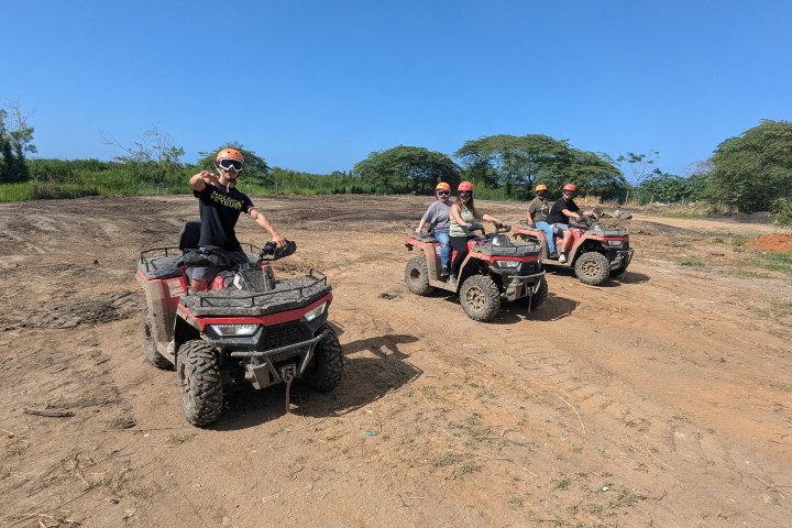 Four people on ATVs in a dirt field under a clear sky.