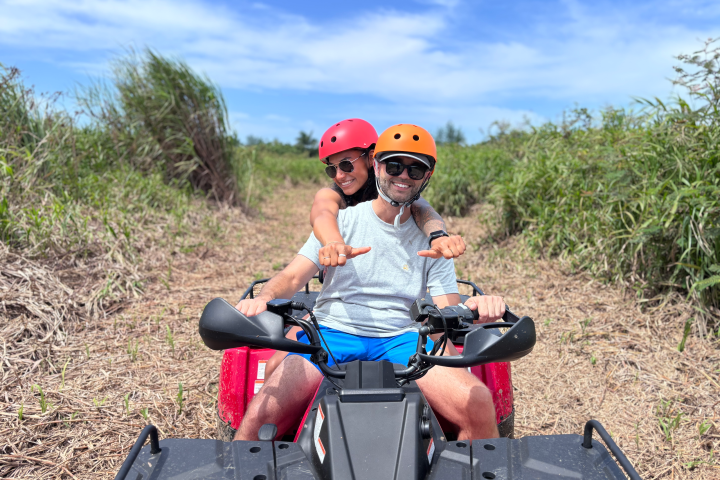 Two people in helmets riding an ATV on a grassy path.
