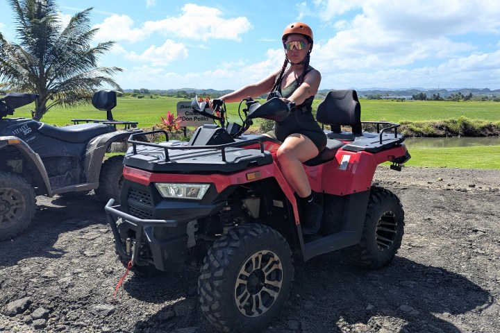 Person on a red ATV with helmet, tropical landscape in background.