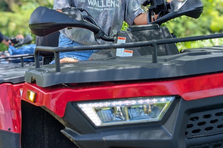 Person wearing a red helmet, sitting on a red ATV, surrounded by lush greenery.