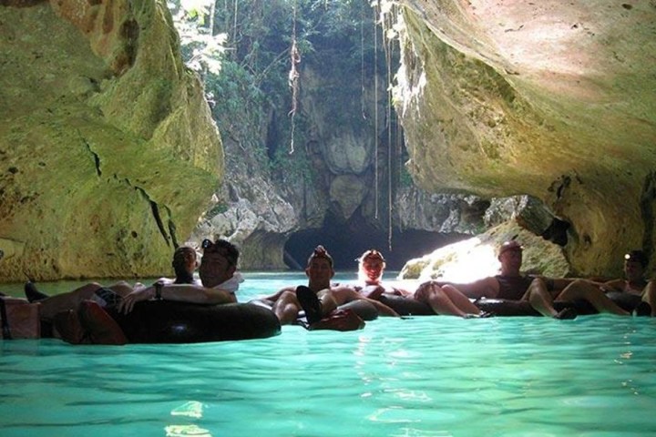 People sitting on inner tubes in a cave with clear turquoise water.