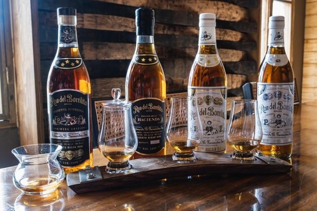 Four bottles of rum and five glasses on a wooden table.