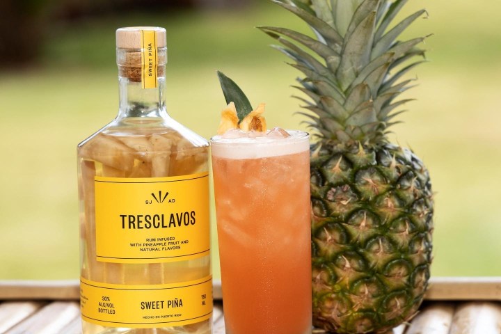 Bottle, pineapple cocktail, and pineapple on a bamboo surface.