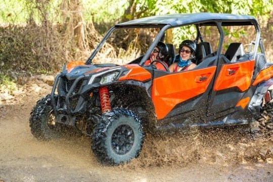 An orange off-road vehicle with two people driving through muddy terrain.