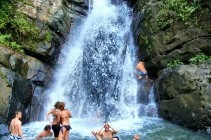 People swimming near a waterfall surrounded by rocks and greenery.