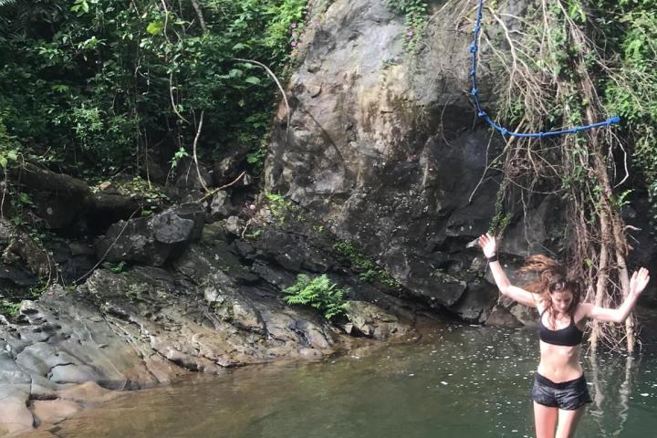 Person swinging on a rope over a river surrounded by lush greenery.